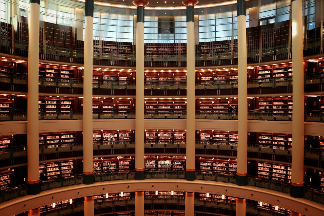 A grand multi-level circular library interior featuring towering columns and warm lighting.