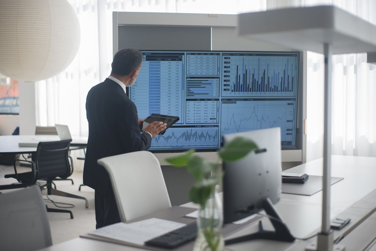 Professional in suit analyzing financial data on screens in a modern office setting.